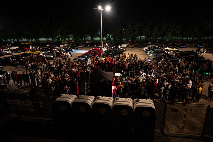 Tłum uczestników nocnego zlotu motoryzacyjnego wśród zaparkowanych aut