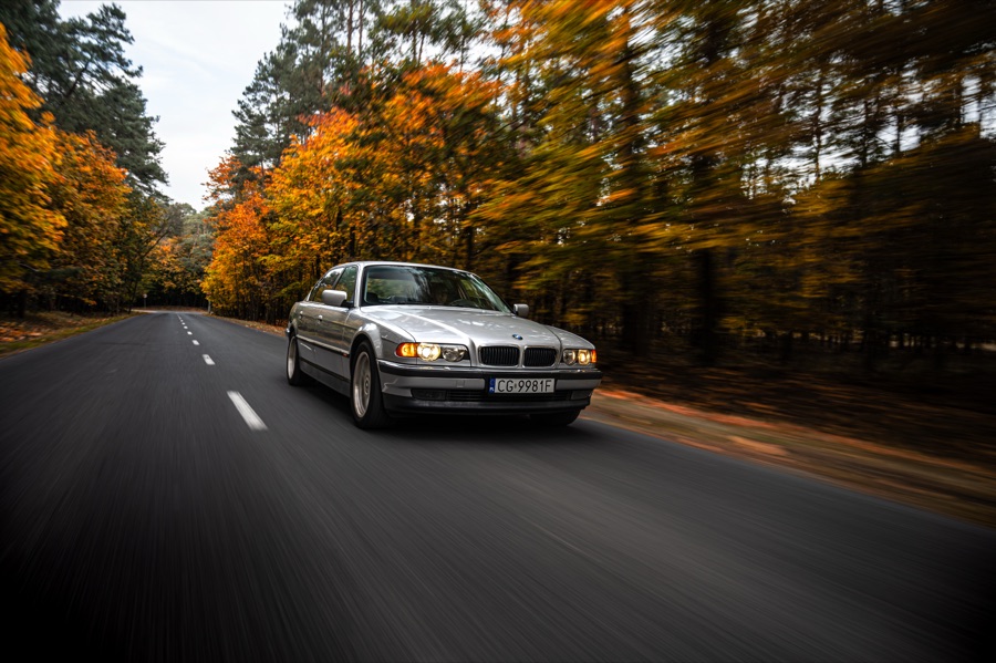 BMW serii 7 jadące jesienną drogą przez las
